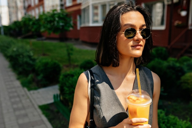 El primer plano de una alegre y bonita chica europea con gafas de sol sonriendo en un fondo oscuro