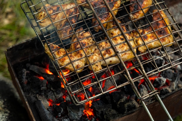 Primer plano de alitas de pollo en rejilla metálica asando a la parrilla en brasero