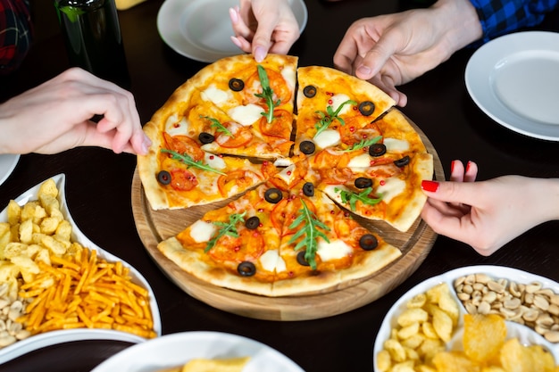 Primer plano de amigos jóvenes guapos bebe cerveza y comiendo pizza en el pub