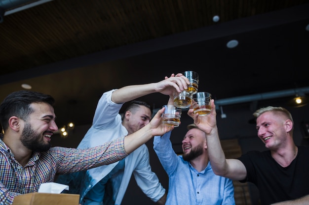 Primer plano de amigos sonrientes tostado vasos de bebidas en el desnudo