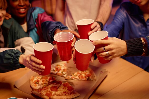 Primer plano de amigos sosteniendo tazas rojas y brindando