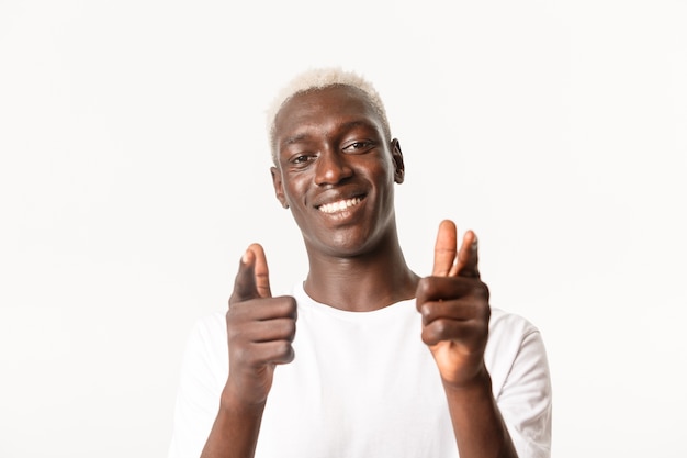 Primer plano de apoyo guapo chico rubio afroamericano señalando con el dedo a la cámara y sonriendo