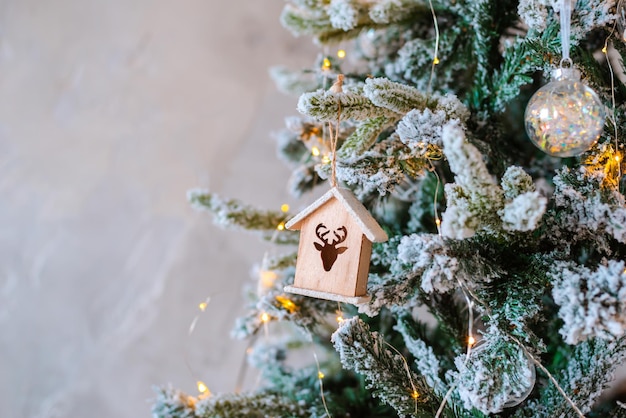 Primer plano de árbol de Navidad cubierto de nieve decorado. Casa de juguete de madera guirnalda iluminada. Adornos navideños Foto macro con bokeh. concepto de decoración de luz de vacaciones de invierno. texto de espacio libre de año nuevo 2020