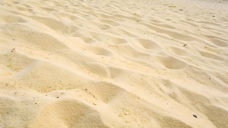 Un primer plano de arena dorada con patrones como olas en una playa soleada