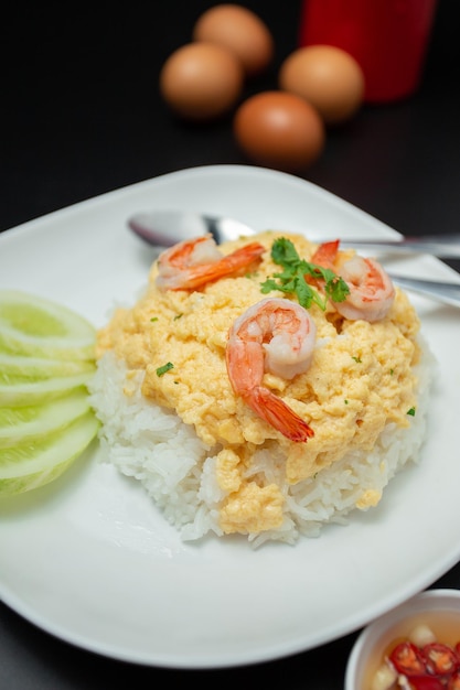 Primer plano de arroz con huevos revueltos encima con camarones en un plato blanco colocado sobre una mesa de madera Desayuno de comida rápida