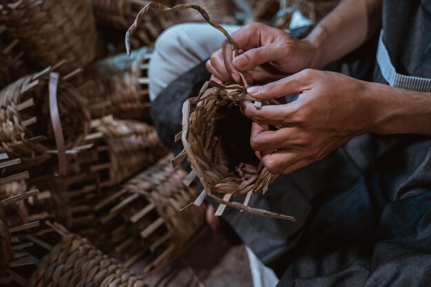 Primer plano de un artesano asiático tejiendo artesanías a mano en un fondo de casa de ladrillo