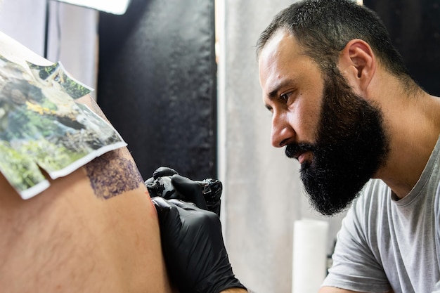 Foto primer plano de un artista tatuando a un cliente en el estudio