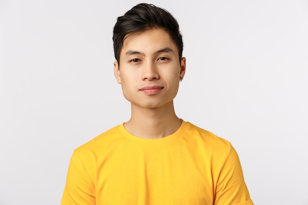 Primer plano asiático encantador, moderno hombre inconformista en camiseta amarilla, sonriendo con expresión segura y asertiva, Newbie comenzando a trabajar en una nueva empresa con ganas de conocer a sus compañeros de trabajo