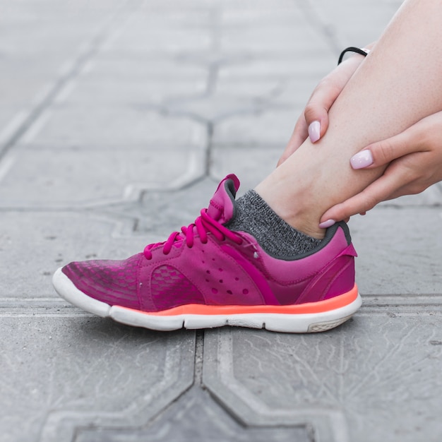 Foto primer plano de atleta femenina con dolor de tobillo en el pavimento de hormigón