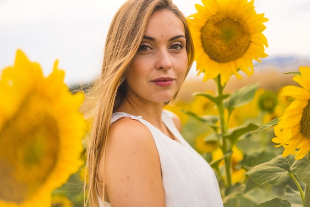 Primer plano de una atractiva modelo rubia con un vestido blanco posando en un campo de girasoles