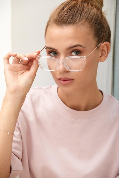 Primer plano de una atractiva mujer rubia europea feliz y exitosa sonriente con reloj de suéter y gafas sonriendo expresando confianza luciendo lograda y atrevida a la cámara con una sonrisa descarada