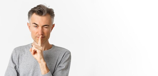 Foto primer plano de un atrevido y guapo hombre de mediana edad guiñando el ojo y haciendo una señal de silencio pidiendo mantener en secreto o persona