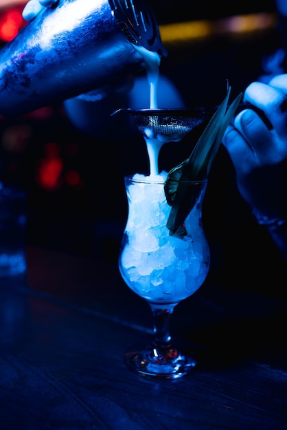 El primer plano del barman vierte un batido en un vaso con hielo Refresco alcohólico ligero azul en una discoteca