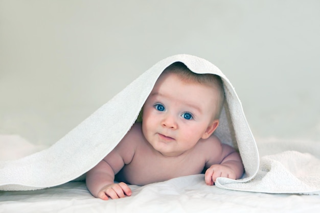 Primer plano de un bebé de cuatro meses con una toalla blanca de ojos azules brillantes en la cabeza de un niño