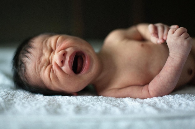 Primer plano de un bebé recién nacido llorando mientras está acostado en la cama en casa