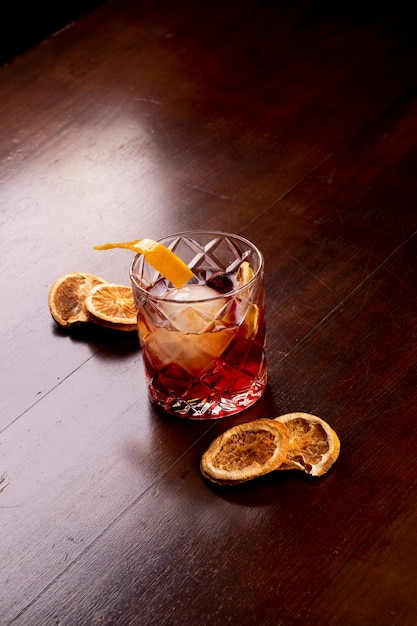 Primer plano de bebida de cóctel Negroni con naranjas deshidratadas en retrato de mesa de madera