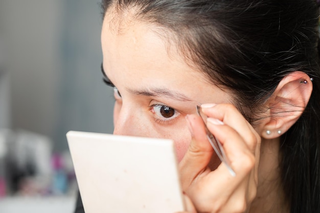 Foto primer plano de una bella adolescente latina depilándose las cejas con un par de pinzas