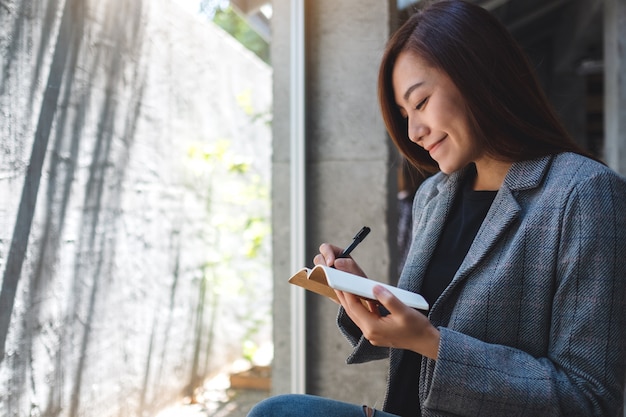 Primer plano de una bella empresaria asiática sosteniendo y escribiendo en un cuaderno