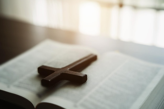 Primer plano de una biblia abierta con una cruz para la devoción matutina en una mesa de madera con luces de ventana