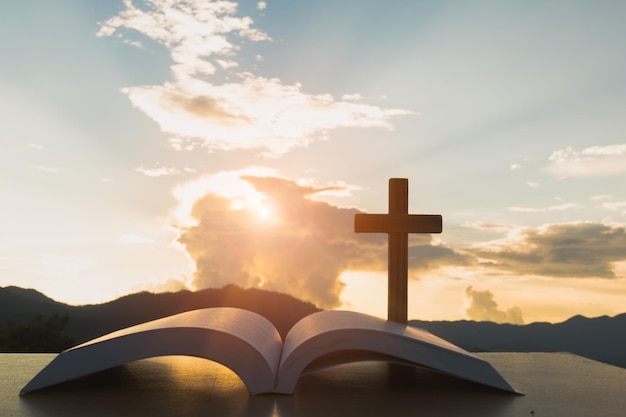 Primer plano de la Biblia con cruz contra el cielo durante la puesta de sol