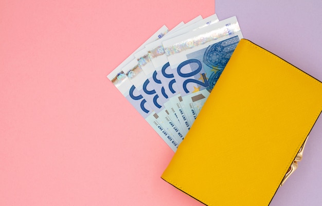 Primer plano de la billetera amarilla con billetes en euros sobre un fondo coloreado