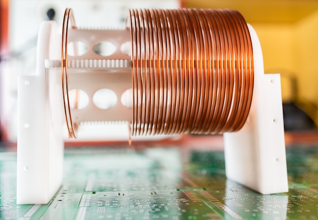 Primer plano de una bobina de alambre de cobre de pie sobre un gran microcircuito con el telón de fondo de los equipos electrónicos modernos. Potente circuito oscilatorio y componentes de alta frecuencia.