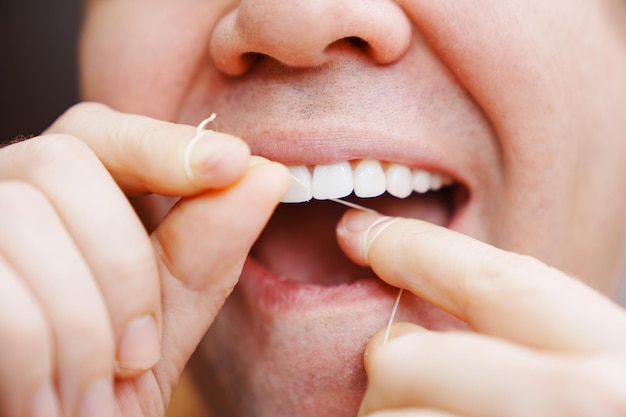 Un primer plano de la boca de un hombre, un hombre se cepilla los dientes con hilo dental