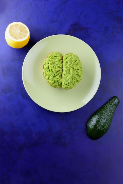 Primer plano de un bocadillo saludable sobre un fondo azul Dos tostadas vegetarianas con aguacate y limón en un plato verde Vista desde arriba