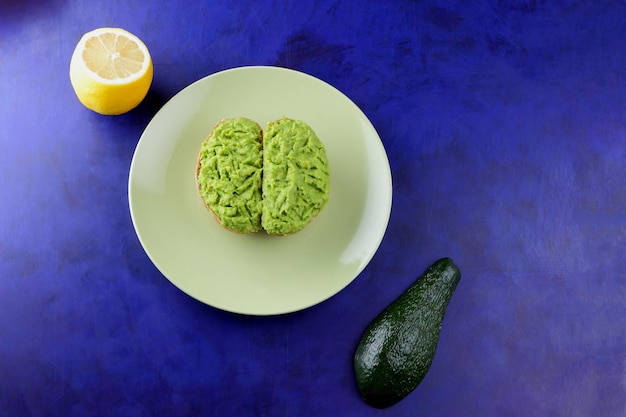 Primer plano de un bocadillo saludable sobre un fondo azul Dos tostadas vegetarianas con aguacate y limón en un plato verde Vista desde arriba