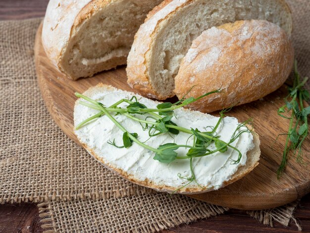 Primer plano de un bodegón hecho de pan crujiente fresco Una rebanada de pan untada con requesón y decorada con micro vegetación Servilleta de lino fondo de madera marrón vista superior endecha plana