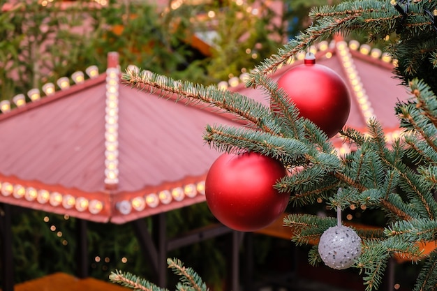Primer plano de bolas de Navidad rojas y guirnaldas en las ramas del árbol de año nuevo natural en el mercado de la ciudad decorada festivamente al aire libre en el día de invierno. No hay gente, no hay nieve.