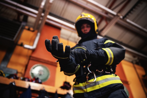 Primer plano de bombero poniéndose guantes y preparándose para la acción mientras está de pie en la estación de bomberos.