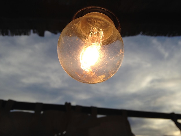 Foto primer plano de una bombilla iluminada contra el cielo al anochecer