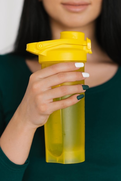 Primer plano de una botella de agua amarilla en manos de una niña después de un entrenamiento