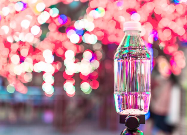 Foto primer plano de una botella de agua en un trípode contra luces iluminadas por la noche