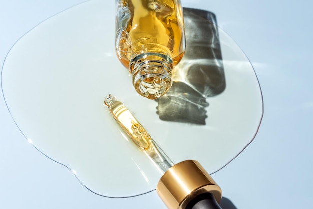 Primer plano de botella cosmética con pipeta y aceite esencial derramado sobre pipeta de vidrio azul y líquido cosmético con burbujas de aire o