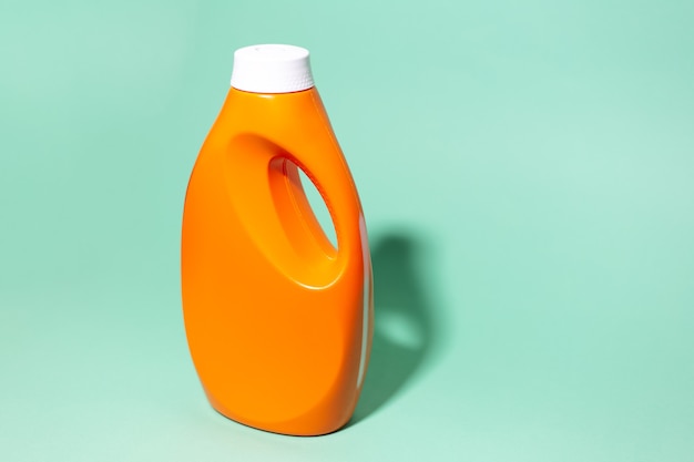 Primer plano de la botella de detergente naranja en la pared de color aqua menthe.