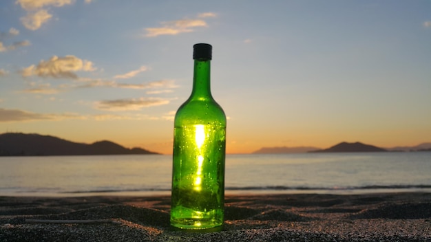 Primer plano de una botella en la orilla de la playa contra el cielo durante la puesta de sol