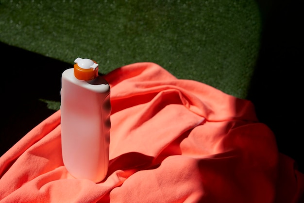Foto primer plano de una botella de protector solar sobre una toalla naranja sobre el césped