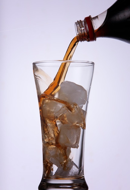 Foto primer plano de una botella vertiendo cola en un vaso contra un fondo blanco