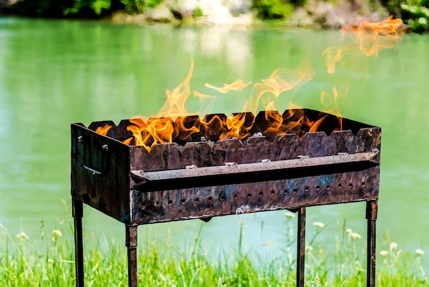 Primer plano de un brasero de metal con fuego en un fondo de río soleado de verano Concepto de camping