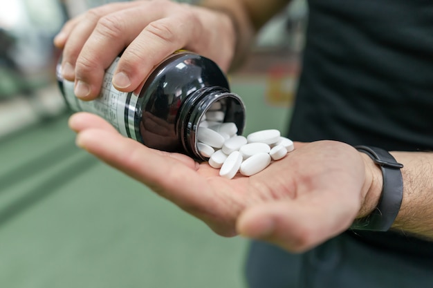 Foto primer plano de los brazos del hombre mostrando suplementos deportivos, cápsulas, píldoras