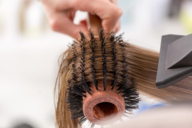 Primer plano de un cabello castaño secado con secador de pelo y cepillo redondo.