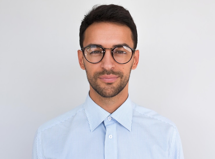 Foto primer plano en la cabeza de un hombre guapo y atractivo que mira directamente a la cámara lleva gafas redondas aisladas sobre fondo blanco retrato de un estudiante de cerdas inteligentes con una camisa azul casual gente
