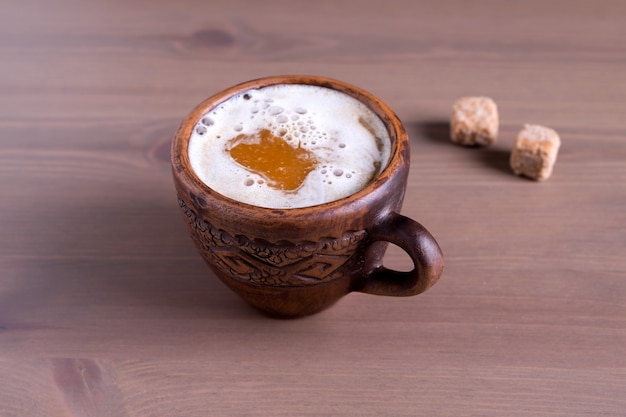 Primer plano de café caliente con leche en una taza de barro cocido con trozos de azúcar de caña. Fondo de madera natural.