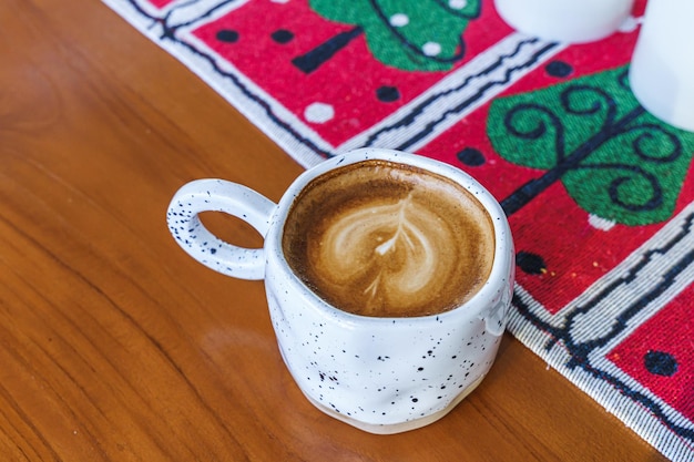 Primer plano de café con leche caliente con espuma de leche de arte latte en una taza con adornos navideños y adornos de árboles de Navidad en el escritorio de madera Celebrando Feliz Navidad y Año Nuevo
