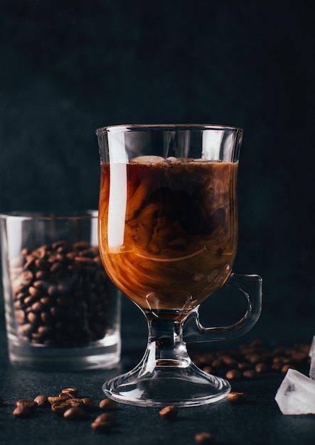 Primer plano de café con leche en un vaso transparente contra el fondo de granos de café sobre un fondo negro