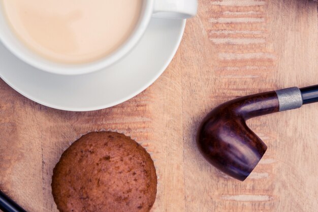 Primer plano de café con muffin y pipa de fumar en mesa