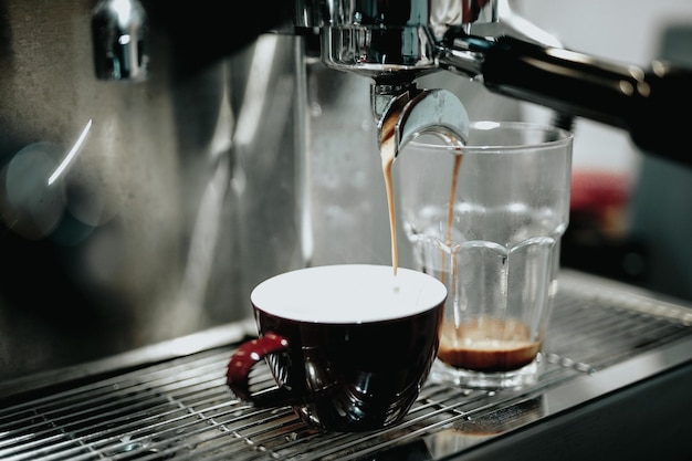 Primer plano del café que se vierte en la taza y el vaso de beber