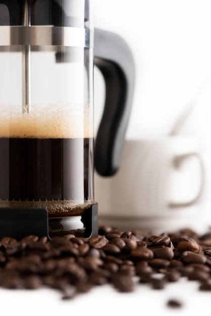 Primer plano de la cafetera con taza de café con leche en la vista frontal del fondo de los granos de café